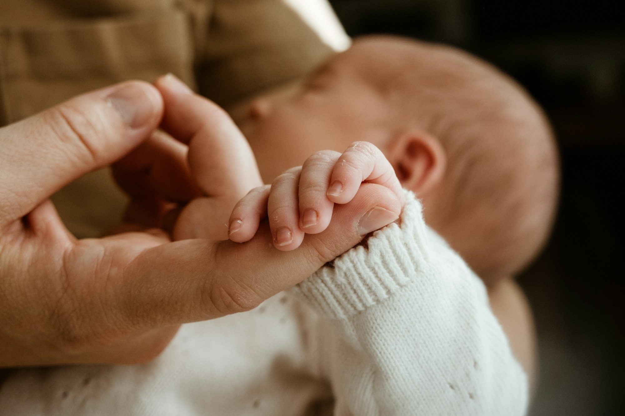 A newborn's hand holding a parent's finger